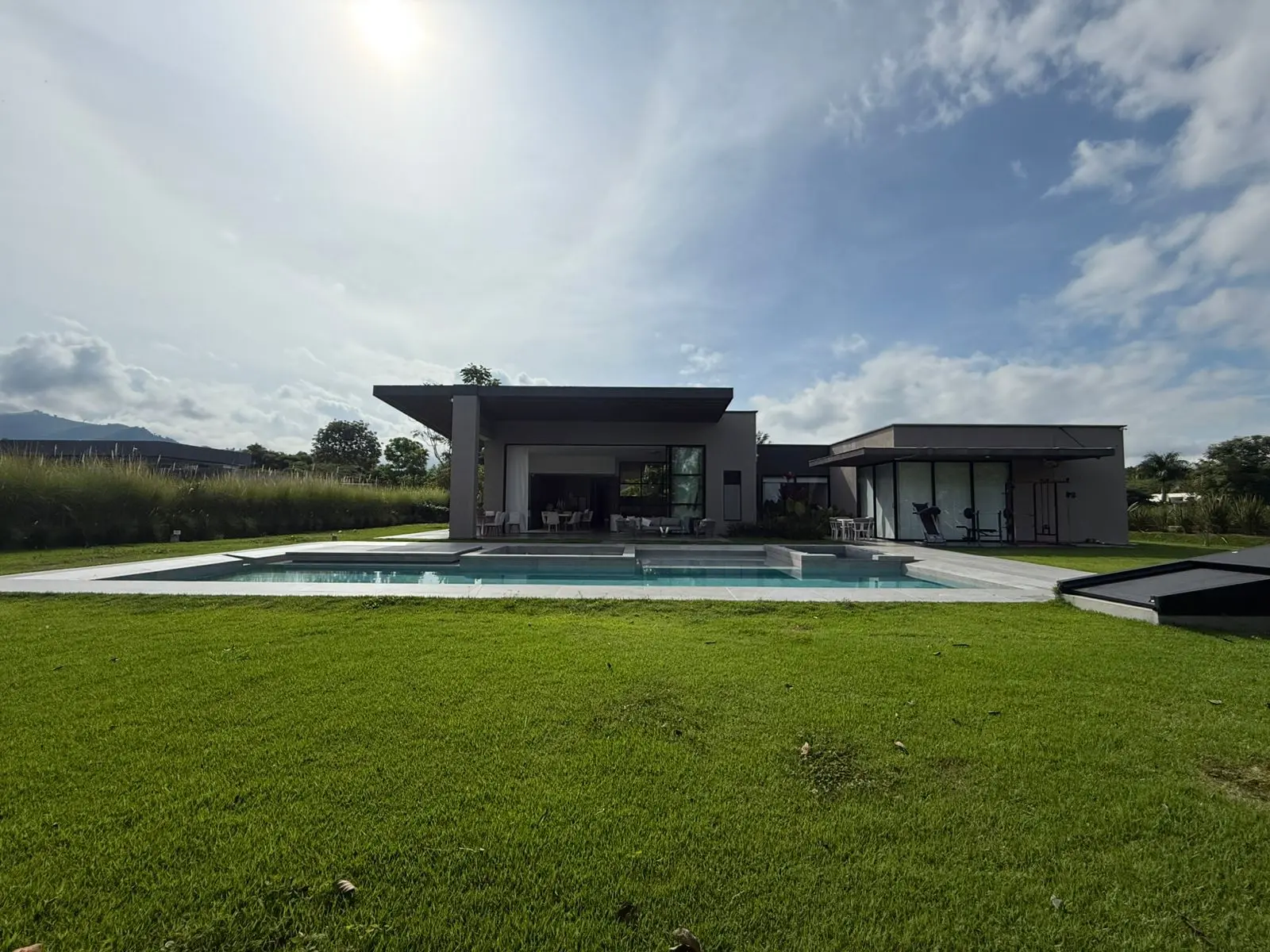 Vista de la casa desde el fondo del jardín, con la piscina y las montañas
